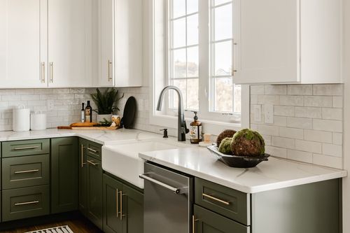 Kitchen sink with farmhouse basin, black faucet and sage cabinetry near a window