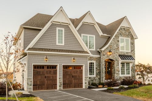 Front exterior of a custom stone and shingle home with a covered porch at dusk in Neffsville