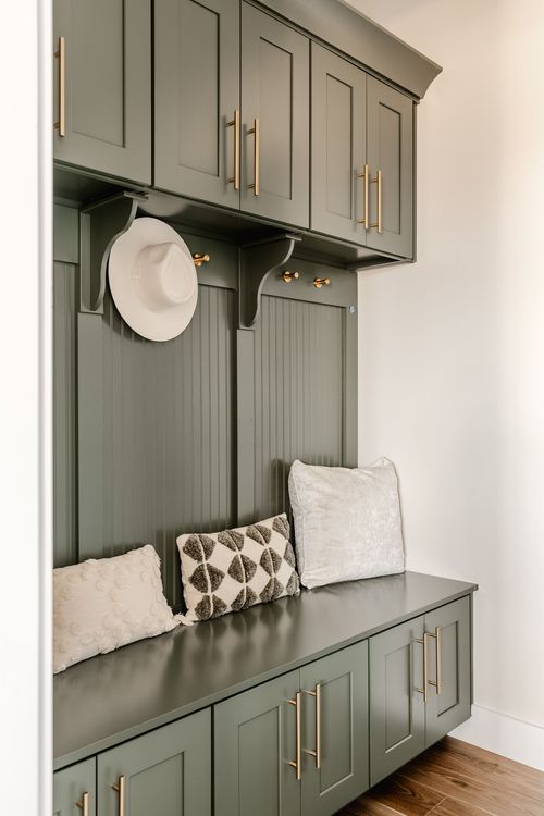 Mudroom nook with sage green cabinetry, hat hooks and a cushioned bench