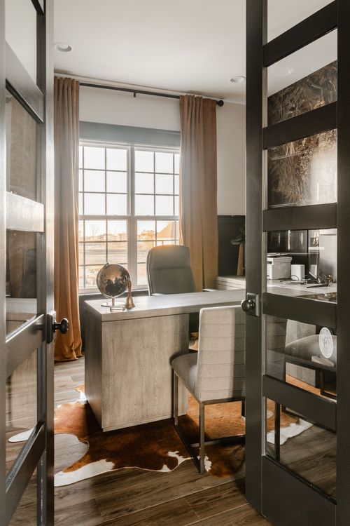Home office with glass-paneled black doors, wood desk and cowhide rug
