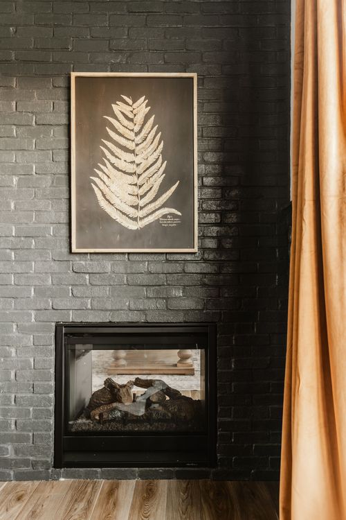 Black brick fireplace with framed botanical art and mustard curtain