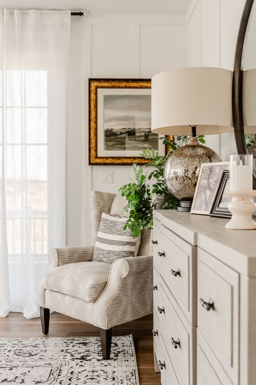 Bedroom sitting corner with striped armchair, framed art and dresser with round mirror