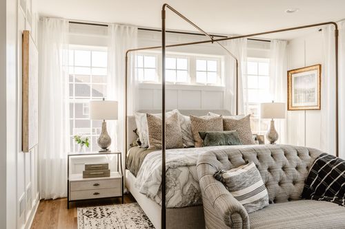 Bedroom with gold canopy bed frame, layered pillows and tufted bench