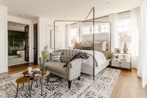 Bedroom with canopy bed, tufted loveseat and doorway to an ensuite bath