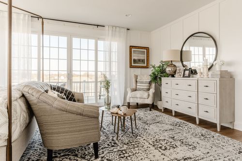 Bedroom sitting area with striped armchair, round mirror and white dresser