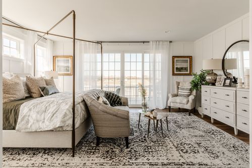 Bedroom with canopy bed, tufted loveseat and framed art beside a private balcony