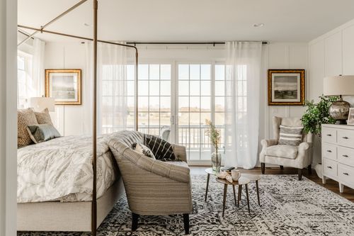 Bedroom with canopy bed and cream armchair overlooking a walkout balcony
