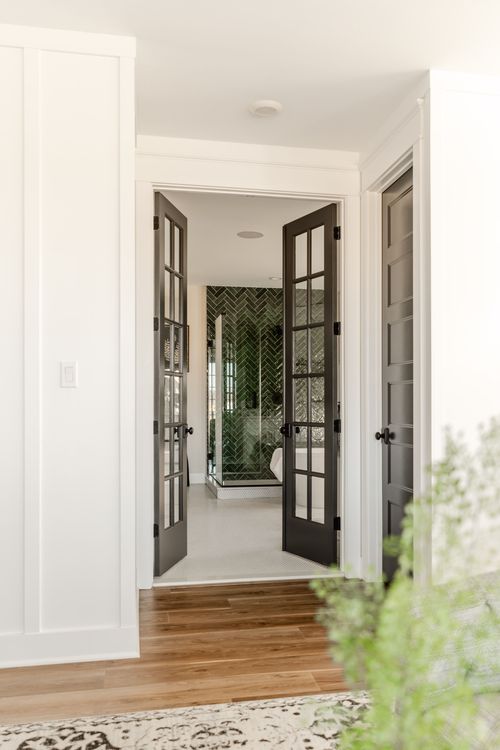 Entry to an ensuite bathroom with black French doors and green herringbone tile beyond