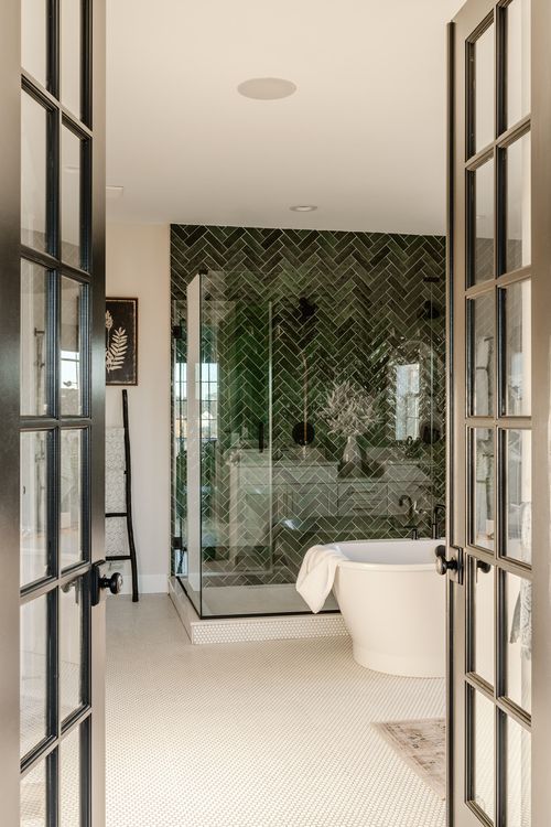 Bathroom with green herringbone tile shower wall, glass enclosure and freestanding tub