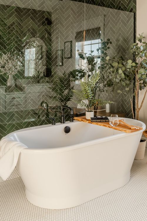 Freestanding white soaking tub with black fixtures and a wood tray against green tile