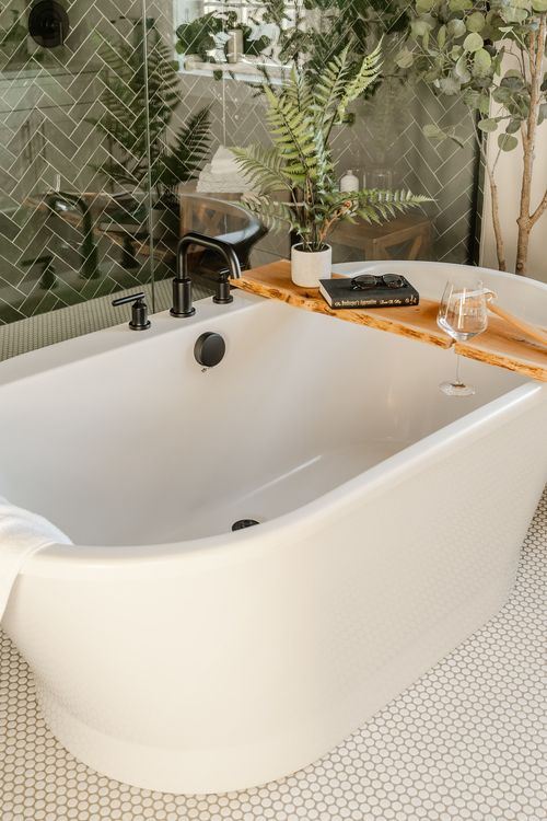 Close-up of a freestanding tub with black faucet, wood caddy and ferns