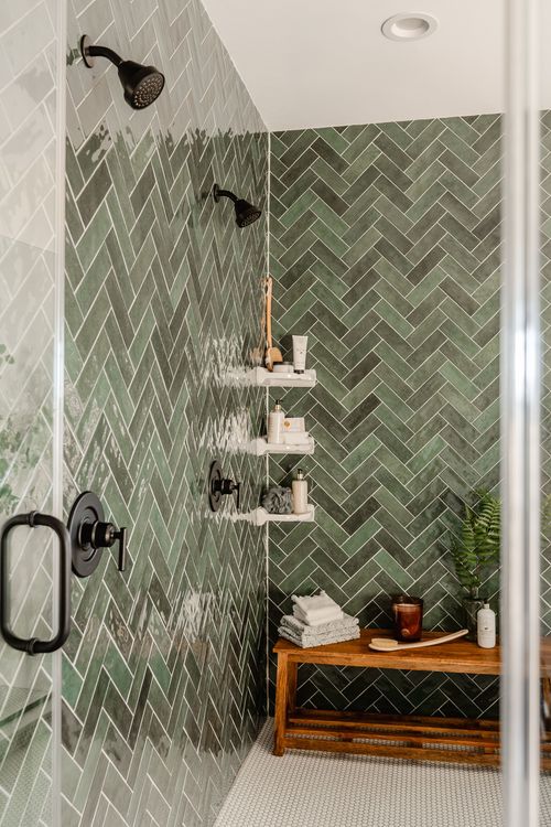 Walk-in shower with green herringbone tile, black fixtures and built-in shelving