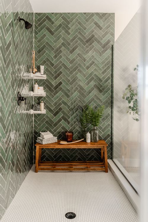 Walk-in shower with green herringbone tile and a wood bench beneath dual showerheads