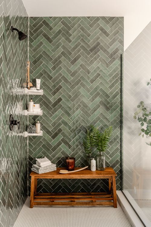 Shower corner with green herringbone tile, wood bench and towel shelving