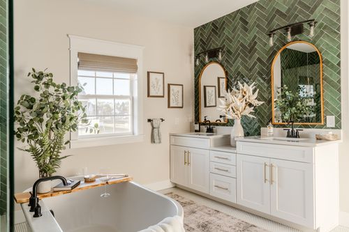 Primary bathroom with double vanity, arched mirrors and green herringbone accent wall