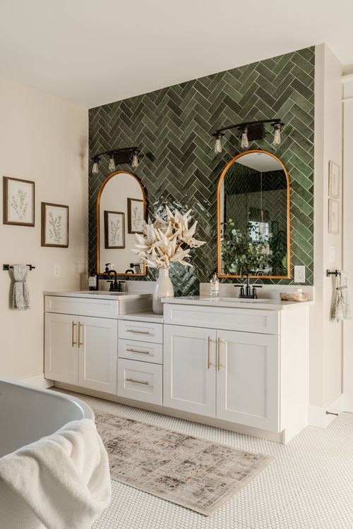 Bathroom double vanity with gold-framed arched mirrors and green herringbone tile