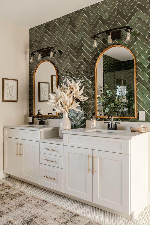 Close-up of a white double vanity with gold hardware and green herringbone tile backdrop