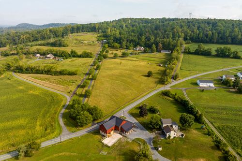 Aerial view of a farmhouse and outbuildings surrounded by open fields and a circular driveway