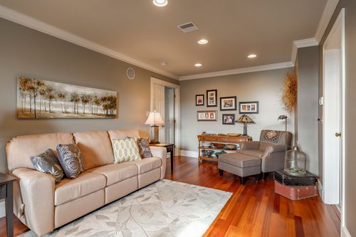 Family room with a tan sofa, framed tree-print artwork, and hardwood floors