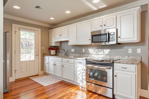 White kitchen with granite counters, stainless range and microwave, and hardwood flooring