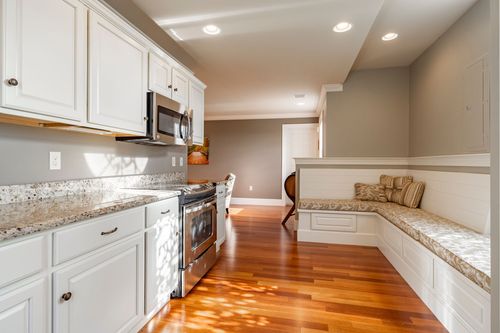 White kitchen with granite countertops and stainless appliances opens to a built-in banquette