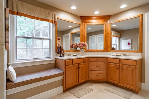 Corner bathroom vanity with wood cabinetry and a cushioned bay-window seat