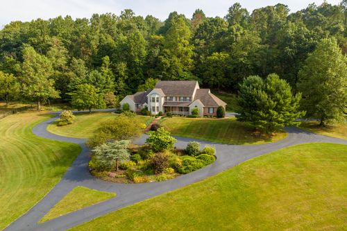 Aerial view of a two-story home with a circular driveway and surrounding woodland