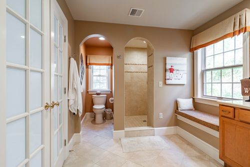 Primary bath hallway with a tiled shower stall, arched doorway, and a window bench