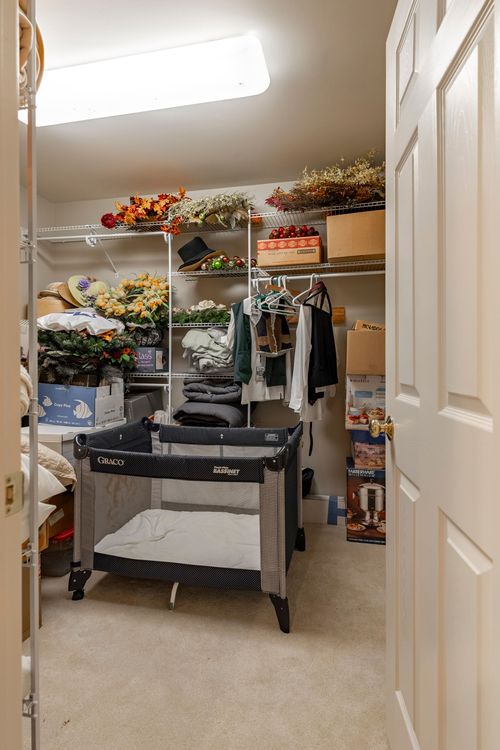 Walk-in closet with wire shelving, hanging clothes, and a portable crib