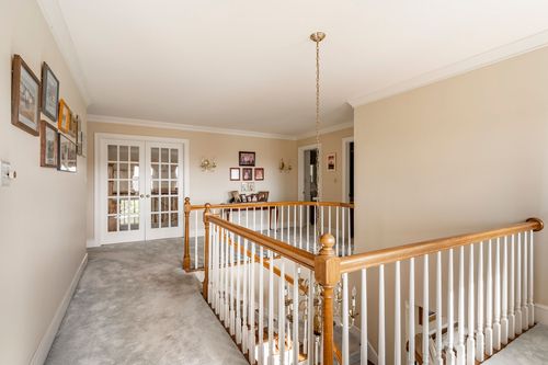 Upstairs landing with wood-capped white balusters, French doors, and a gallery of framed photos