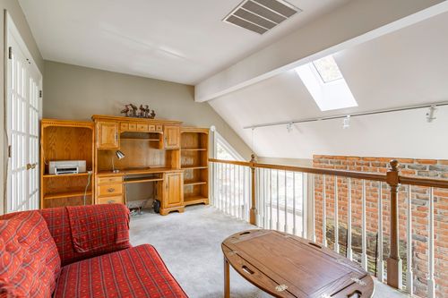 Loft office nook with an oak desk, brick railing, and red plaid upholstered seating