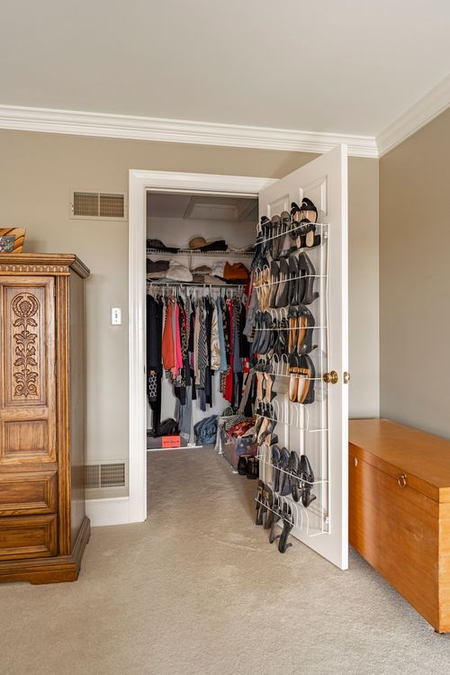 Walk-in closet with hanging clothes, over-door shoe racks, and a wood dresser