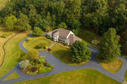 Aerial view of a home with a curved driveway, landscaped island and wooded backdrop