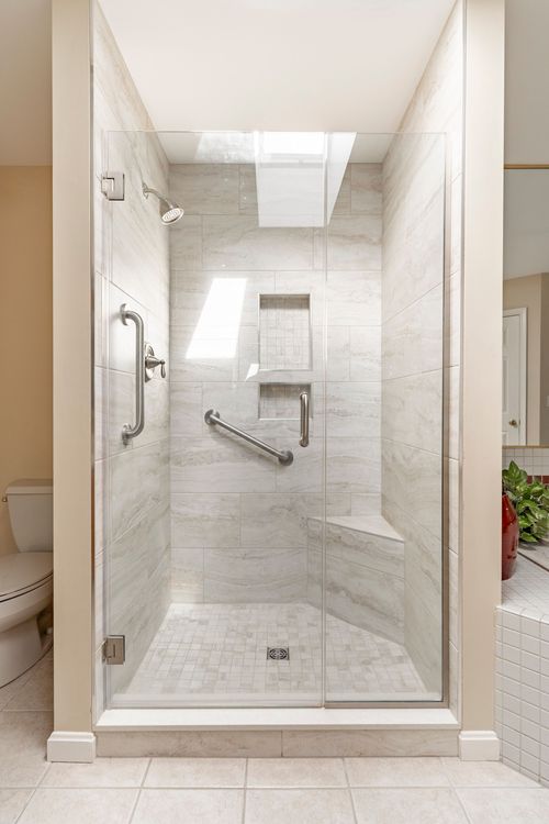 Glass-enclosed shower with a skylight, built-in tile bench, and dual grab bars