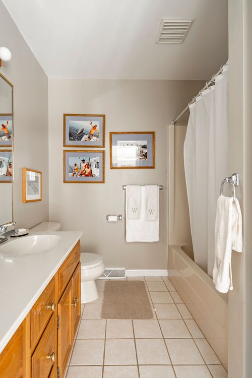 Bathroom with framed sailing photos, monogrammed towels, and a tub-shower combo
