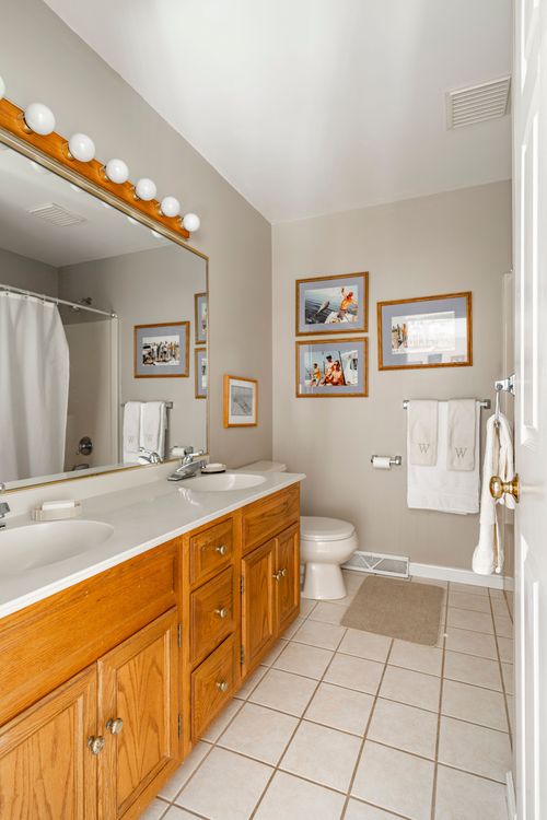 Bathroom with a Hollywood-style vanity light bar, dual sinks, and framed beach photos