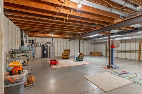Unfinished basement with exposed wood joists, a mini basketball hoop, and play rugs