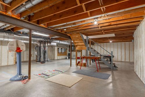 Unfinished basement rec space with a mini basketball hoop, ping pong table, and open staircase