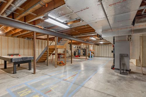 Unfinished basement with an air hockey table, wood staircase, and painted court lines on the floor