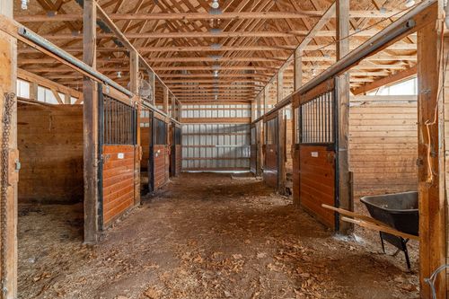 Wood barn aisle lined with horse stalls and a wheelbarrow