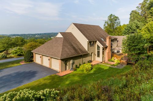 Aerial view of a two-story home with a stone chimney and wooded hillside setting