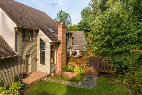 Aerial view of a home's back deck and stone patio surrounded by trees