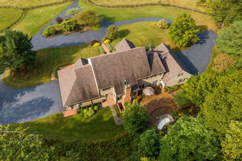 Aerial view of a home with a curved driveway and fenced pasture along a wooded property line