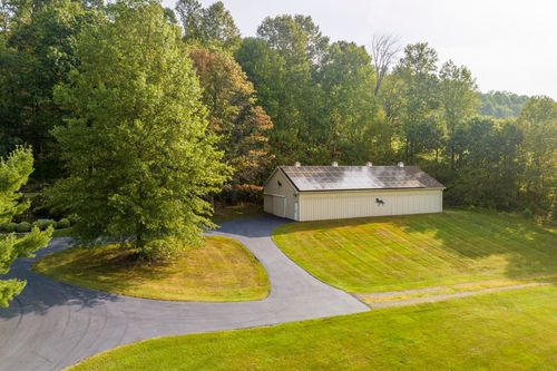 Aerial view of a pole barn with solar panels set near a tree-lined driveway