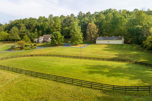 Aerial view of a farmhouse and barn with a fenced oval pasture in the foreground