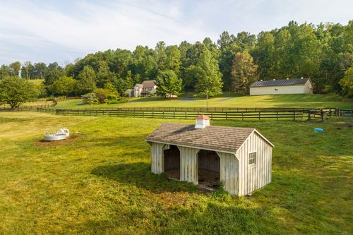 Aerial view of a wood shed with a cupola set in an open pasture near a fenced pole barn