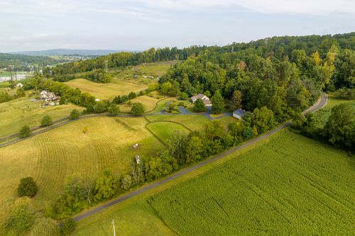 Aerial view of rolling farmland with a house, pond and country road winding through fields