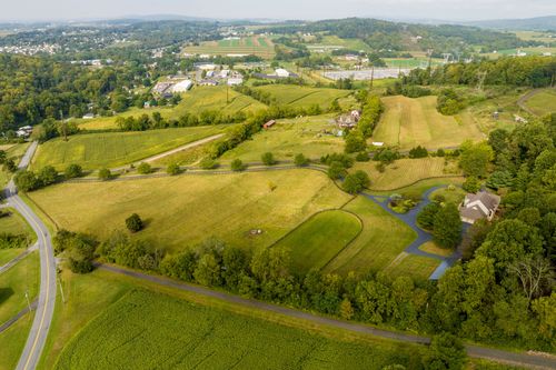 Aerial view of a property with a pond and stream framed by pastures and distant hills