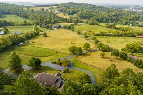 Aerial view of a home with a curved driveway set among rolling pastures and a distant barn