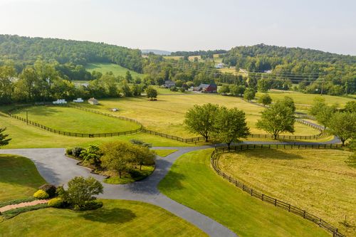 Aerial view of a fenced pasture with a tree-lined driveway leading to a red barn